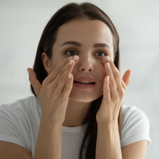 Woman applying cream to her face with a neutral background