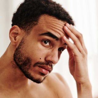Man with a beard and mustache touching his forehead against a neutral background