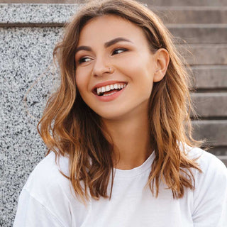 Woman with shoulder-length brown hair wearing a white shirt against a stone wall.