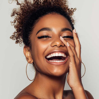 Woman with a big smile touching her face against a neutral background