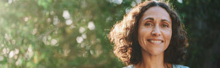 Woman with curly hair smiling outdoors with a blurred green background