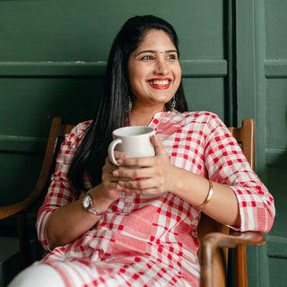 Woman in a red and white checkered outfit holding a white mug against a green wall.