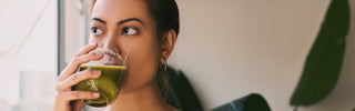 Woman drinking green juice indoors with a plant in the background