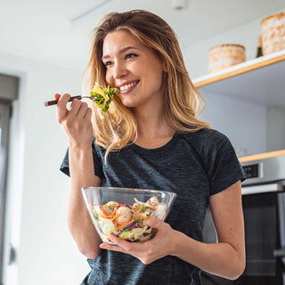 Woman holding a bowl of salad and a fork with a smile in a kitchen.
