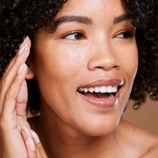Woman with a happy expression, touching her face with one hand.