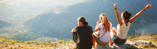 Three people sitting on a mountain overlooking a scenic landscape with mountains and valleys.